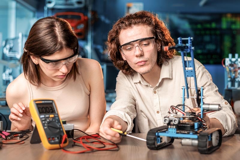 Junge Männer und Frauen mit Schutzbrille machen Experimente zur Robotik